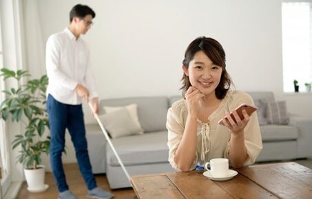 掃除する夫とスマホをみる妻