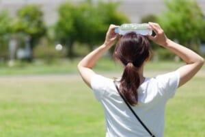 水のペットボトルで頭を冷やす女性