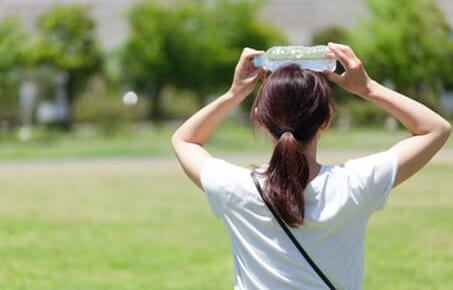 水のペットボトルで頭を冷やす女性