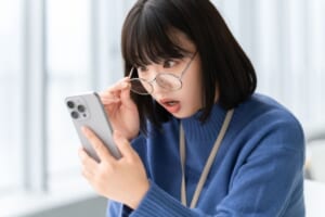 スマホの画面を見て驚く女性